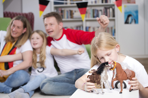 Familie sieht sich die Fußballweltmeisterschaft im Fernsehen an, während das kleine Mädchen mit Spielzeug spielt, lizenzfreies Stockfoto