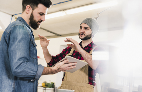 Zwei Männer mit Tablet diskutieren in einer Werkstatt, lizenzfreies Stockfoto