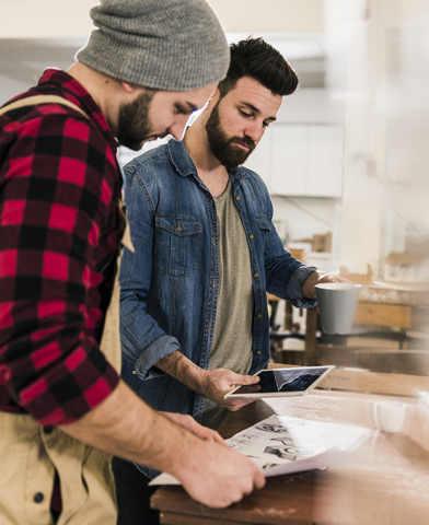 Zwei Männer mit Tablet betrachten einen Entwurf in einer Werkstatt, lizenzfreies Stockfoto