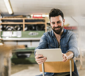 Smiling man sitting on chair in workshop - UUF12687