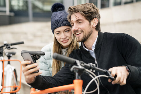 Lächelndes Paar mit Fahrrädern und Mobiltelefon in der Stadt - PESF00995