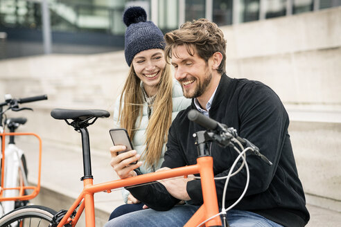 Lächelndes Paar mit Fahrrädern und Mobiltelefon in der Stadt - PESF00996