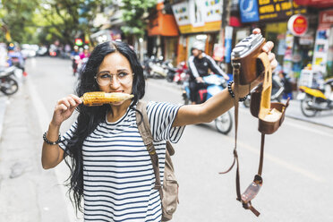 Vietnam, Hanoi, junge Frau macht ein Selfie mit altmodischer Kamera auf der Straße und isst einen Maiskolben - WPEF00063