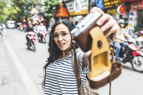 Vietnam, Hanoi, junge Frau macht ein Selfie mit altmodischer Kamera auf der Straße, lizenzfreies Stockfoto