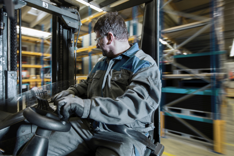 Fork-lift driver in motion in storehouse stock photo