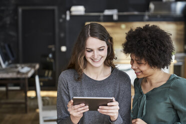 Two smiling young women sharing tablet in office - FMKF04796