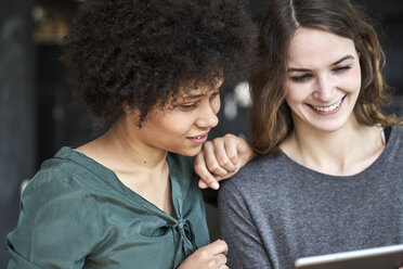 Zwei lächelnde junge Frauen teilen sich ein Tablet - FMKF04797