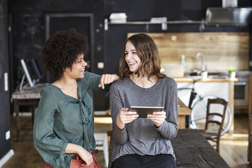 Zwei lachende junge Frauen mit Tablet im Büro - FMKF04798