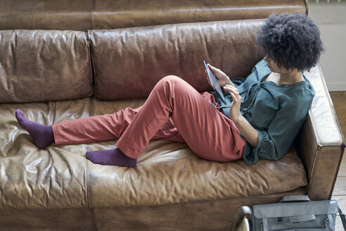 Junge Frau auf Couch liegend mit Tablet - FMKF04801