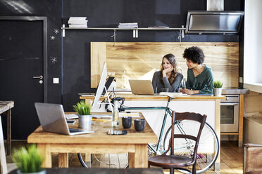 Zwei junge Frauen benutzen einen Laptop in einem modernen Büro - FMKF04804