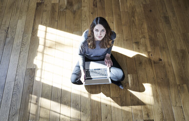 Porträt einer jungen Frau, die einen Laptop auf einem Holzboden benutzt - FMKF04808