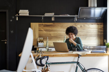 Young woman using laptop on kitchen counter - FMKF04812