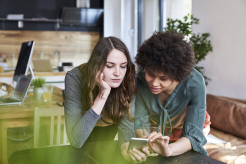 Zwei junge Frauen teilen sich ein Mobiltelefon in einem modernen Büro - FMKF04816