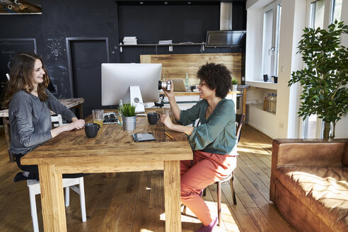 Zwei glückliche junge Frauen mit Kamera in einem modernen Büro - FMKF04818