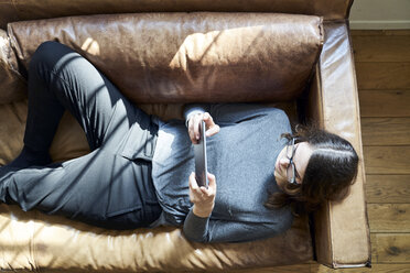 Young woman lying on couch using tablet - FMKF04821