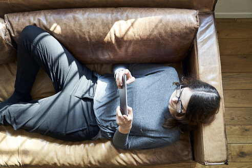 Junge Frau auf Couch liegend mit Tablet - FMKF04821