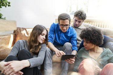 Young people sitting on sofa looking at tablet - FMKF04836