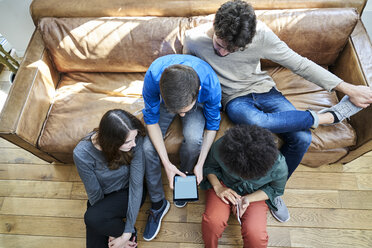 Junge Leute sitzen auf dem Sofa und schauen auf ein Tablet - FMKF04837