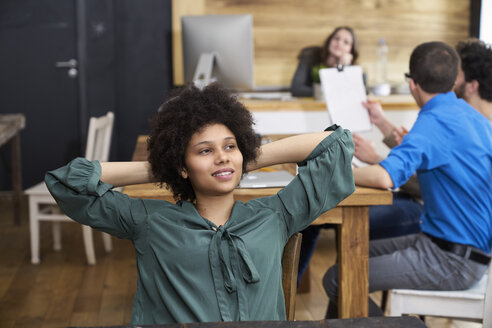 Junge Frau, die im Büro nachdenkt, mit Arbeitskollegen im Hintergrund - FMKF04850