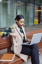 Geschäftsfrau sitzt auf einer Bank und benutzt einen Laptop - MAUF01322