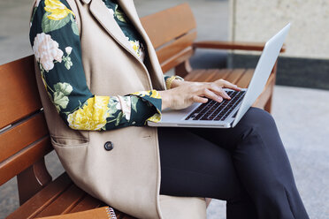 Businesswoman sitting on bench using laptop, partial view - MAUF01323