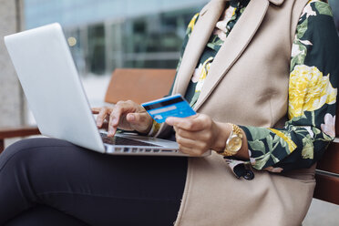 Businesswoman sitting on bench using laptop and credit card, partial view - MAUF01324