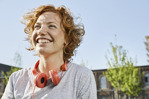 Porträt einer glücklichen jungen Frau mit Kopfhörern in städtischer Umgebung - PDF01419