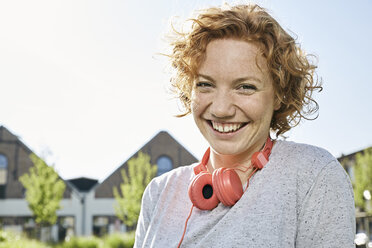 Portrait of happy young woman with headphones in urban surrounding - PDF01422