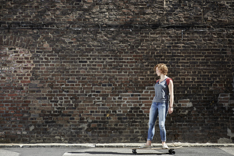 Junge Frau fährt mit Longboard an einer Mauer entlang, lizenzfreies Stockfoto