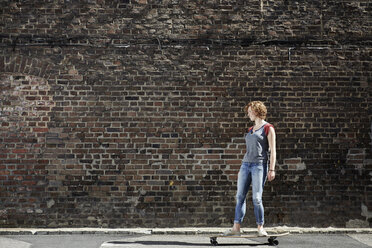 Junge Frau fährt mit Longboard an einer Mauer entlang - PDF01429