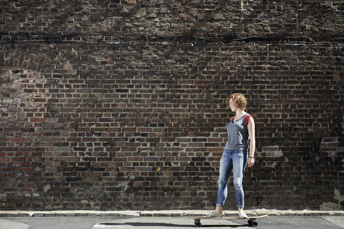 Young woman riding along brick wall with longboard - PDF01429