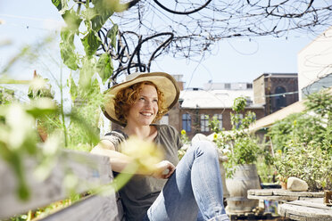 Lächelnde junge Frau mit Strohhut entspannt sich in einem städtischen Garten - PDF01438