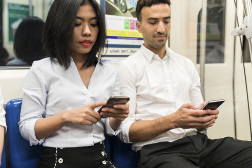 Geschäftsmann und Geschäftsfrau benutzen Handys in der U-Bahn - WPEF00089