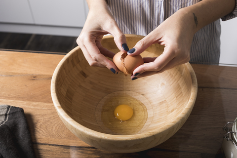 Woman breaking egg, wooden bowl stock photo