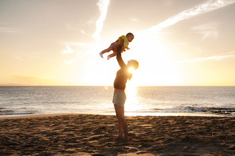 Mother lifting up little daughter on the beach at sunset stock photo