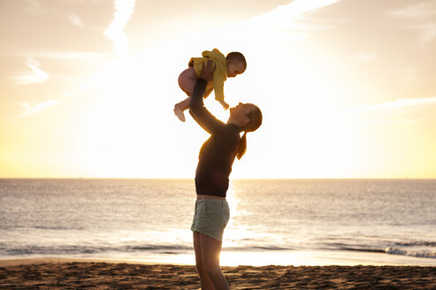 Mother lifting up little daughter on the beach at sunset - DIGF03239