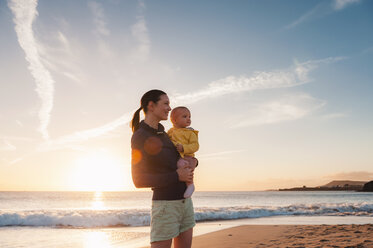 Mutter hält kleine Tochter am Strand bei Sonnenuntergang - DIGF03244