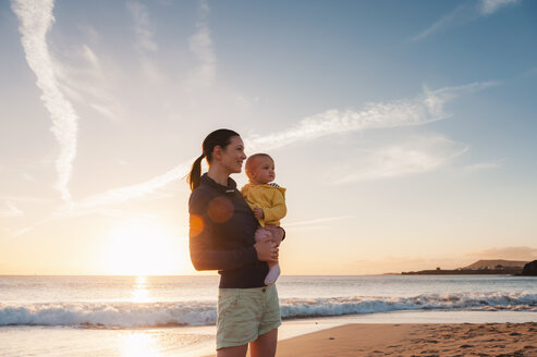 Mother holding little daughter on the beach at sunset - DIGF03244