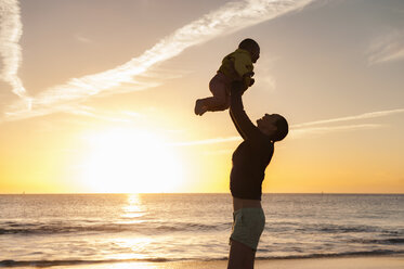 Mutter hebt kleine Tochter am Strand bei Sonnenuntergang hoch - DIGF03245