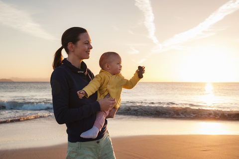 Mother holding little daughter on the beach at sunset stock photo