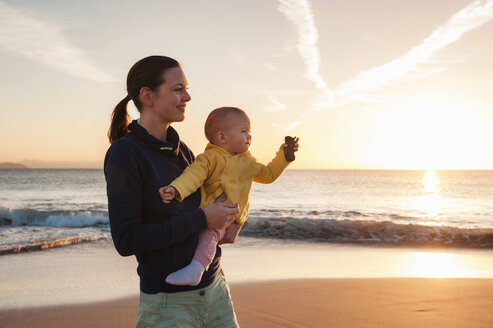 Mother holding little daughter on the beach at sunset - DIGF03246