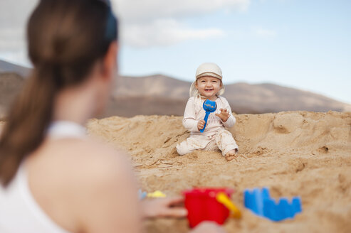 Happy baby girl playing on the beach looking at mother - DIGF03254