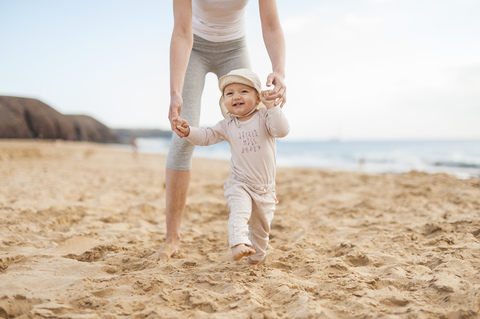 Mother helping little daughter walking on the beach stock photo