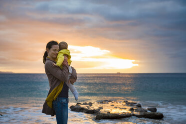 Mutter hält kleine Tochter am Strand bei Sonnenuntergang - DIGF03268