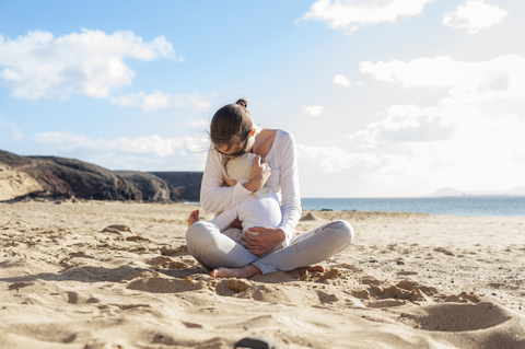 Mother cuddling with little daughter on the beach stock photo