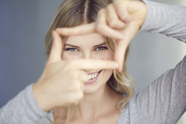 Portrait of laughing woman building frame with her fingers - PNEF00523