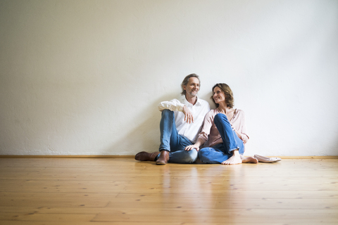 Lächelndes reifes Paar sitzt auf dem Boden in einem leeren Raum, lizenzfreies Stockfoto