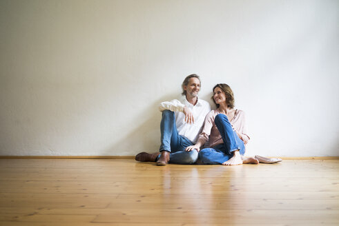 Smiling mature couple sitting on floor in empty room - MOEF00739