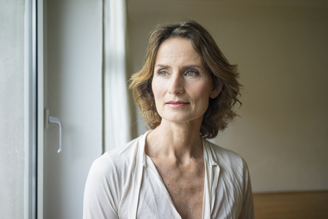 Porträt einer nachdenklichen reifen Frau am Fenster, lizenzfreies Stockfoto