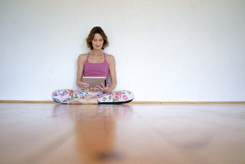 Mature woman sitting on floor in empty room using tablet - MOEF00748